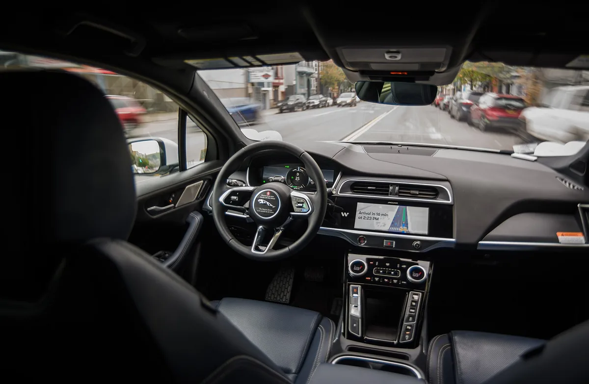 The empty driver’s seat of a Waymo robotaxi moving through traffic, steering wheel turning on its own.