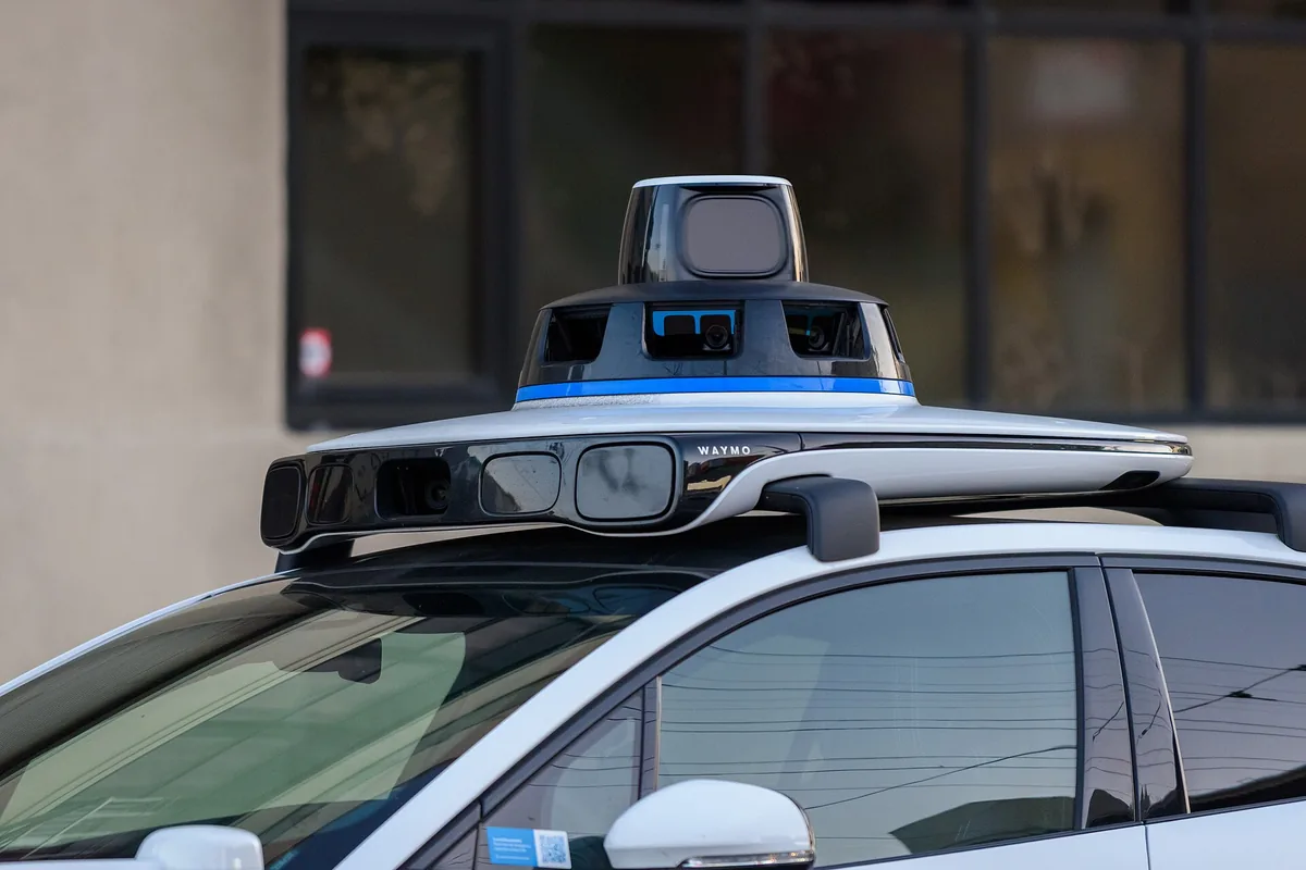 Close-up of the roof sensor unit on a Waymo car, holding cameras and a spinning laser scanner.