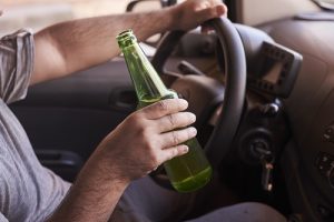 Bottle of beer in a man's hands driving the car during daytime